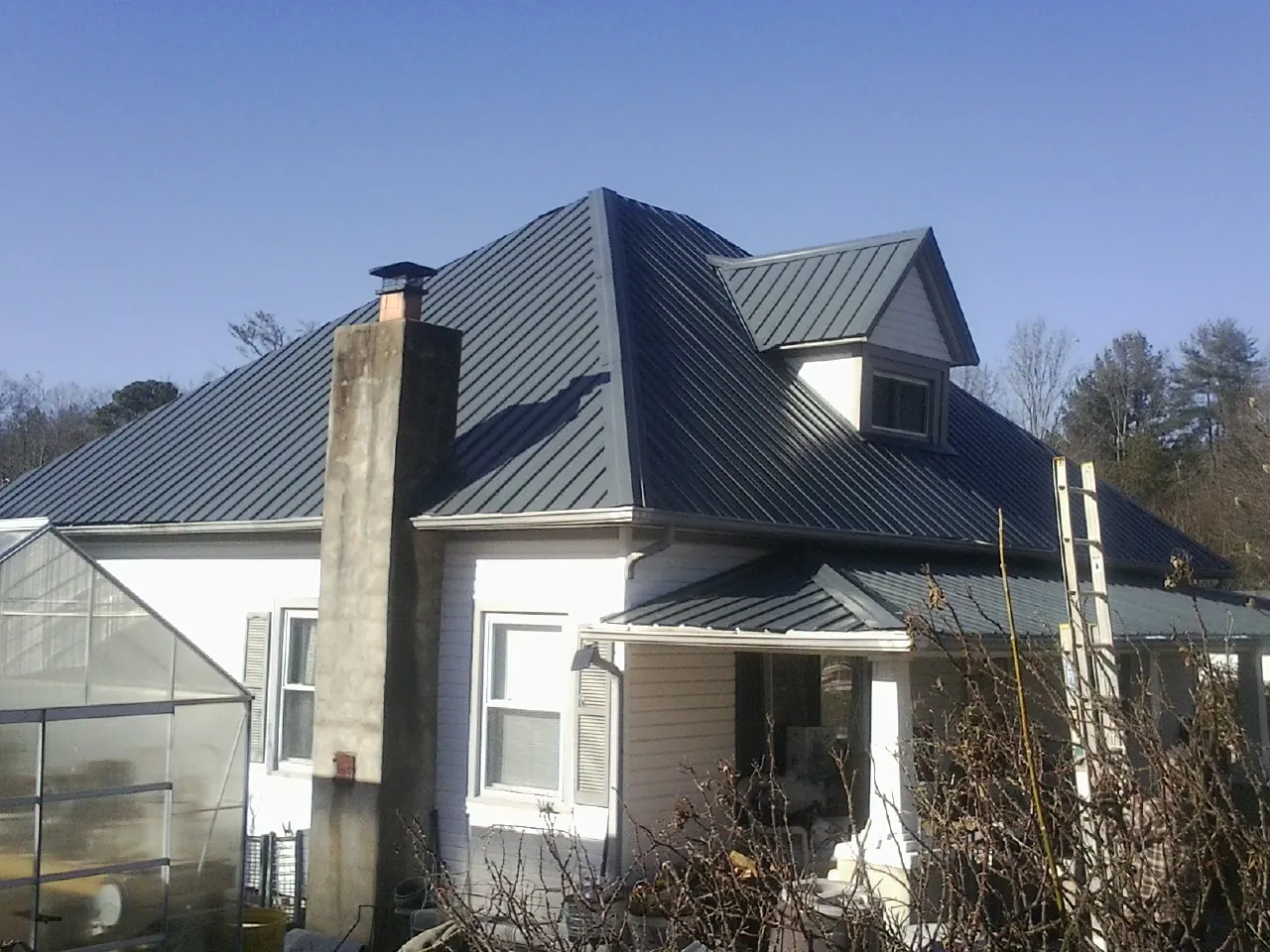 Dark blue standing seam metal roof on a white farmhouse with dormer — Slate & Tile Roof Repair by Roofing Brothers in Allenton