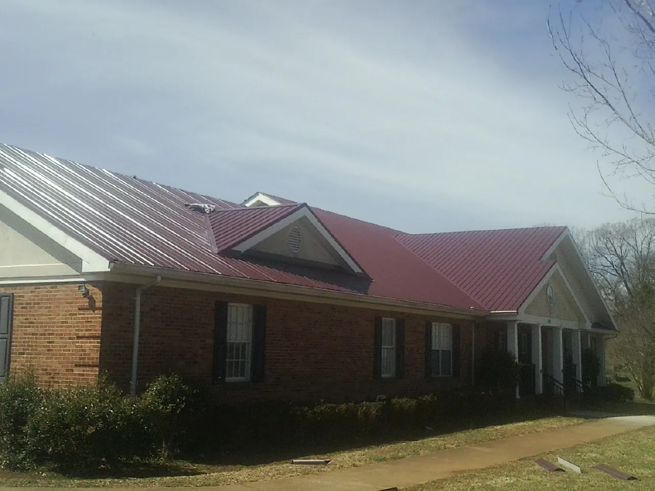 Red metal roof with gabled entries on a long brick building, from a Hail Damage Roof Repair job in Allenton